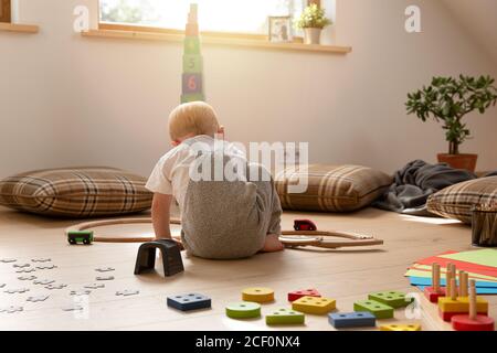 Boy playing on a sunny day in a room with a train surrounded by other toys. Stock Photo