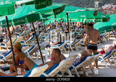 Tourists using umbrellas and sun loungers on the beach at Patong, Phuket, Thailand