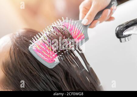 Master applies conditioner to hair using massage comb. Shampooing with special deep cleansing in beauty salon Stock Photo