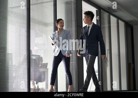 two asian business people on their way to meeting talking while walking in office Stock Photo