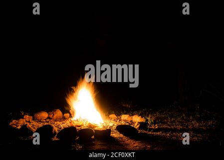 Flames of a campfire in deep darkness surrounded by stones shaping strong shadows. Space for inserting text Stock Photo