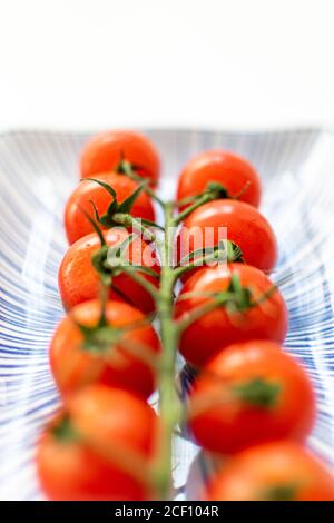 a vine of cherry tomatoes macro and horizontally on a ceramic plate Stock Photo