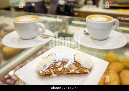 Two cups of cappuccino and fresh ricotta cannoli dessert close-up in coffee bar in Sicily, Italy. Stock Photo