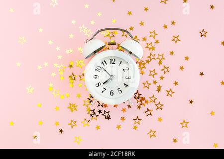Alarm clock covered golden stars confetti, decoration on a pink, festive background. Christmas or New Year pattern. Colorful celebration, birthday. Stock Photo