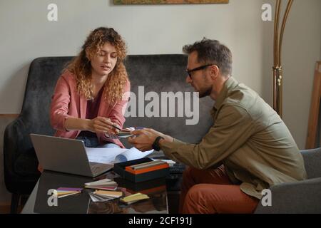 Two designers sitting at the table in front of laptop and examining the colored patterns at office Stock Photo