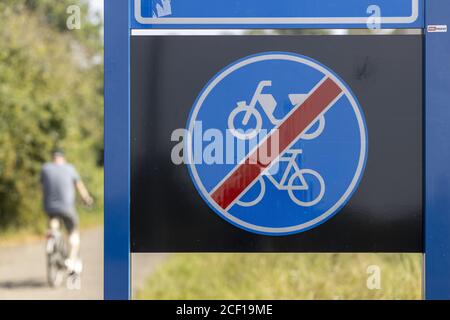 ALMELO, NETHERLANDS - Aug 02, 2020: Dutch traffic sign signifying the end of a bicycle and moped path with a man on a bike and foliage of trees in the Stock Photo