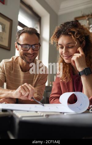 Two smiling architects looking at blueprint of new building and discussing it while sitting at the table at office Stock Photo