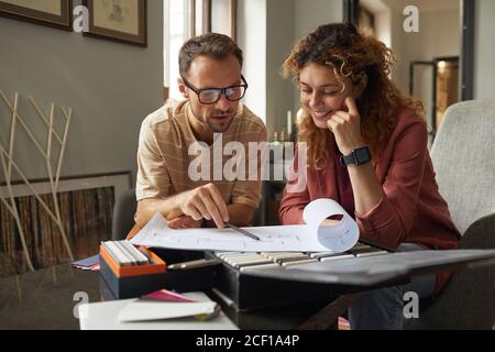 Two architects sitting at the table and discussing blueprint of new building at office Stock Photo