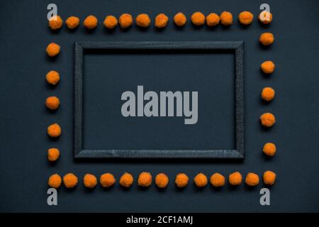 Wooden frame and orange fluffy pom-poms for Halloween with copy space for text on a black background. Flat lay, top view. Festive theme. Mock up. Stock Photo