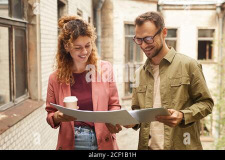 Two successful architects looking at blueprint and using digital tablet while working outdoors Stock Photo
