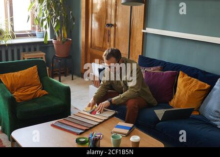 Mature designer in eyeglasses sitting on sofa in front of the table and working with fabric samples at modern office Stock Photo