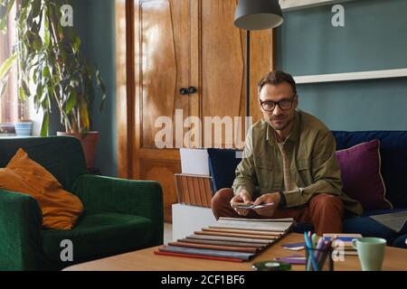 Portait of mature man in eyeglasses looking at camera while working with colored patterns at office Stock Photo