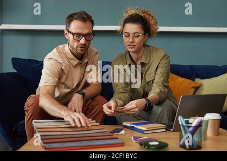 Two designers sitting on sofa and working with fabric samples they discussing new fashion project Stock Photo