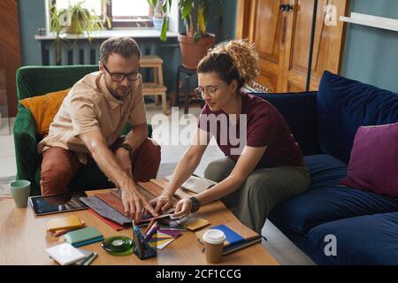 Two designers sitting on sofa and working with samles and patterns in team they choosing the color for new project Stock Photo
