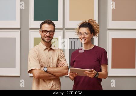 Portrait of two designers working on digital tablet smiling at camera while they standing at art gallery Stock Photo