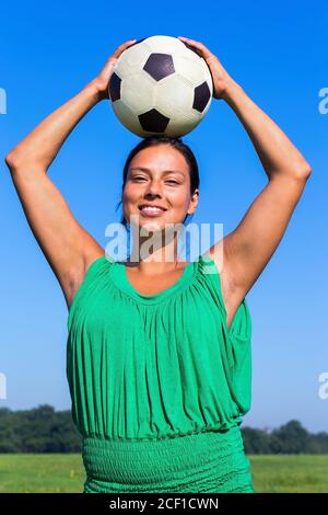 Young Colombian woman holding football on head in blue sky Stock Photo