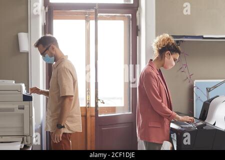Two designers in protective masks working on printed equipments at office they printed papers and documents Stock Photo