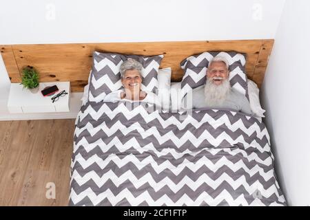 Happy married senior couple lying in bed under blanket looking at camera before going to sleep - Mature people having fun - Elderly love and happiness Stock Photo