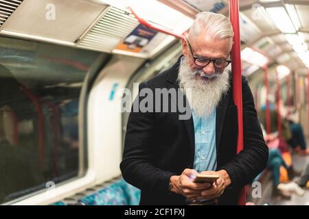 Senior hipster man using smartphone in subway underground - Fashion mature person travels by train and have fun with technology trends - Joyful elderl Stock Photo