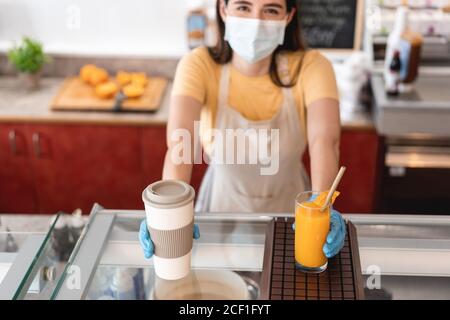 Bar owner giving takeaway orders to customer at her restaurant during corona virus outbreak - Young woman worker wearing face surgical mask giving dri Stock Photo