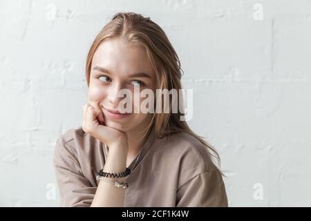 Young smiling blond girl, close-up studio portrait with natural light over white wall Stock Photo
