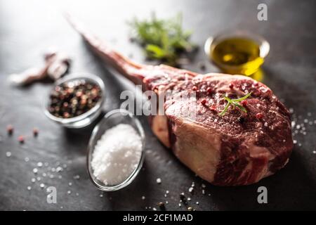 Raw tomahawk steak with salt spices garlic and herbs on a old rustic board Stock Photo