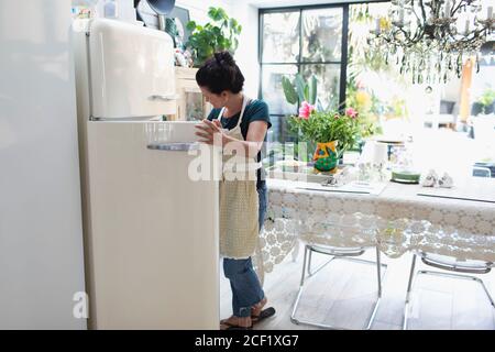 Woman in apron standing at open refrigerator in kitchen Stock Photo