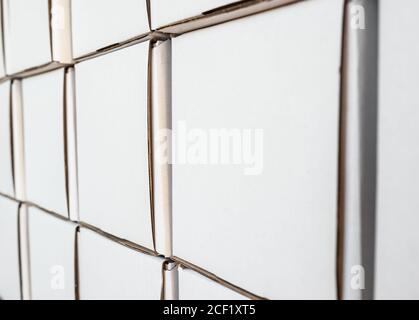 Side view of white paper boxes in rows, minimalistic design objects. Wall with cardboard square shaped empty packages in delivery room, closeup view, Stock Photo