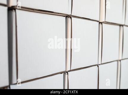Side view of white paper boxes in rows, minimalistic design objects. Wall with cardboard square shaped empty packages in delivery room, closeup view, Stock Photo