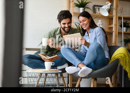 Spending nice time at home. Couple bonding to each other and smiling while reading book, tablet Stock Photo