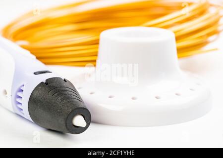 Closeup view of colorful rolled cables and childrens 3D printing pen isolated on white. Three bright filament plastic lying indoors, studio background Stock Photo