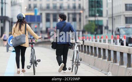 Business people in face masks walking bicycles on city bridge Stock Photo