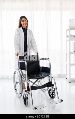 Portrait of confident female doctor medical professional holding wheelchair examination room in hospital clinic.