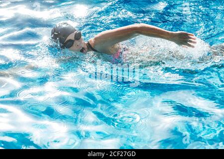 Woman with swimming cap and goggles swimming in a pool.