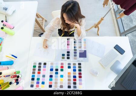 Top view a young adult fashion designer drawing and sketching her work at her atelier studio with colour palette as sole owner. Using for