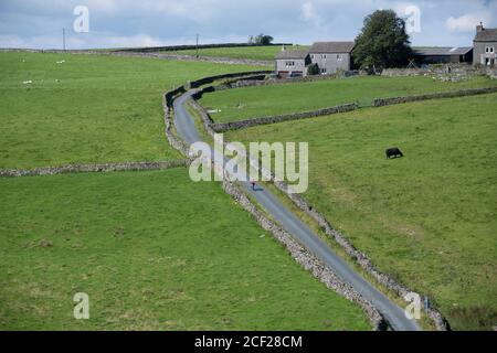 Female cyclist climbing a steep hill on her electric bike in the Yorkshire Dales national park, UK. Stock Photo
