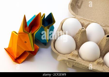 Origami rabbits from colored paper. Easter hares and white chicken eggs in the box Stock Photo