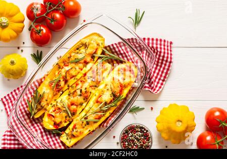 Stewed yellow zucchini with tomatoes and onions, cheese and herbs, carrots and spices, stuffed zucchini on a white wooden background Stock Photo