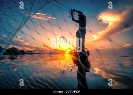 Silhouette Fisherman Fishing Nets on the boat at sunrise in Thailand Stock Photo