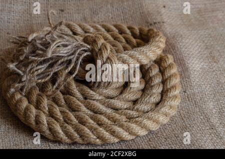 Thick natural rope wound in a reel on sackcloth. Close-up of a laid nautical rope. Marine theme. Selective focus. Stock Photo