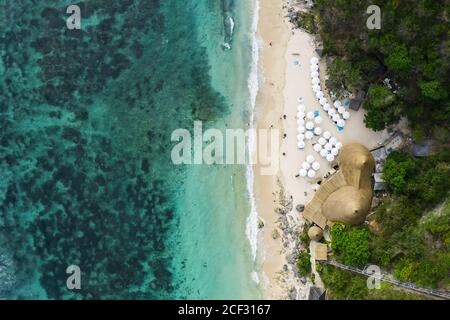View from above, stunning aerial view of some tourists sunbathing on a beautiful beach bathed by a turquoise sea during sunset, Melasti Beach, Bali. Stock Photo