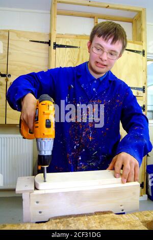 Young man with Downs Syndrome learning how to use drill at a workshop for craftspeople with learning disabilities UK Stock Photo