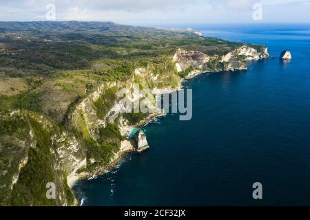 View from above, stunning aerial view of a green limestone cliff bathed by a turquoise sea during sunset. Nusa Penida, Indonesia. Stock Photo