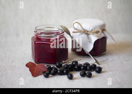 Black currant jam in glass jars. Fresh berries with leaves and stems. Autumn harvesting and preserves. Organic food. Still life photography Stock Photo