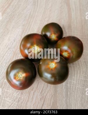 Five fresh, dark red heirloom tomatoes on a wooden table. Stock Photo