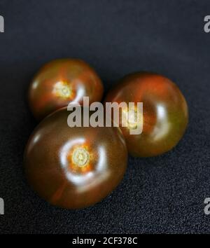 Three fresh, dark red heirloom tomatoes on a black background Stock Photo