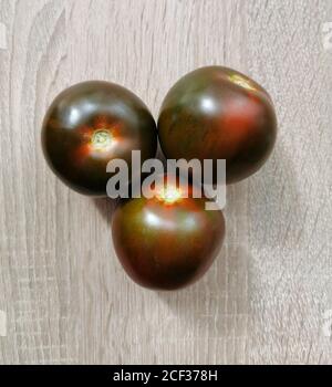 Three fresh, dark red heirloom tomatoes on a wooden table. Stock Photo