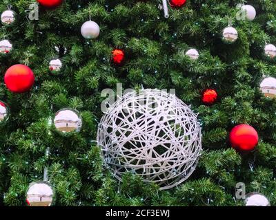 A silver wicker ball entwined with a garland hangs among the spruce branches, red and silver balls and a garland with blue small lights Stock Photo