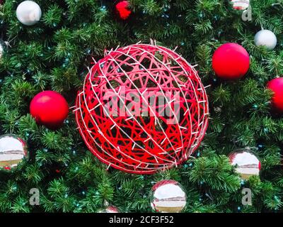 A large red wicker ball entwined with a garland hangs in the center in spruce branches with small red and silver balls around Stock Photo