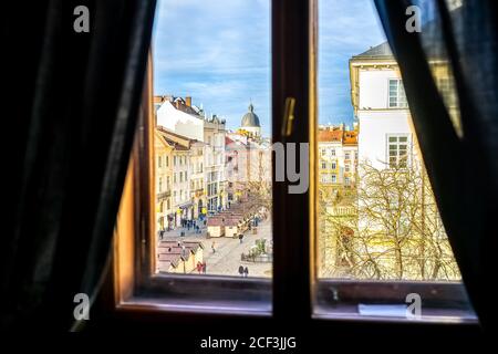 Lviv, Ukraine view of historic Ukrainian city in old town market rynok square with stores and people walking in winter on sunny sunset through window Stock Photo